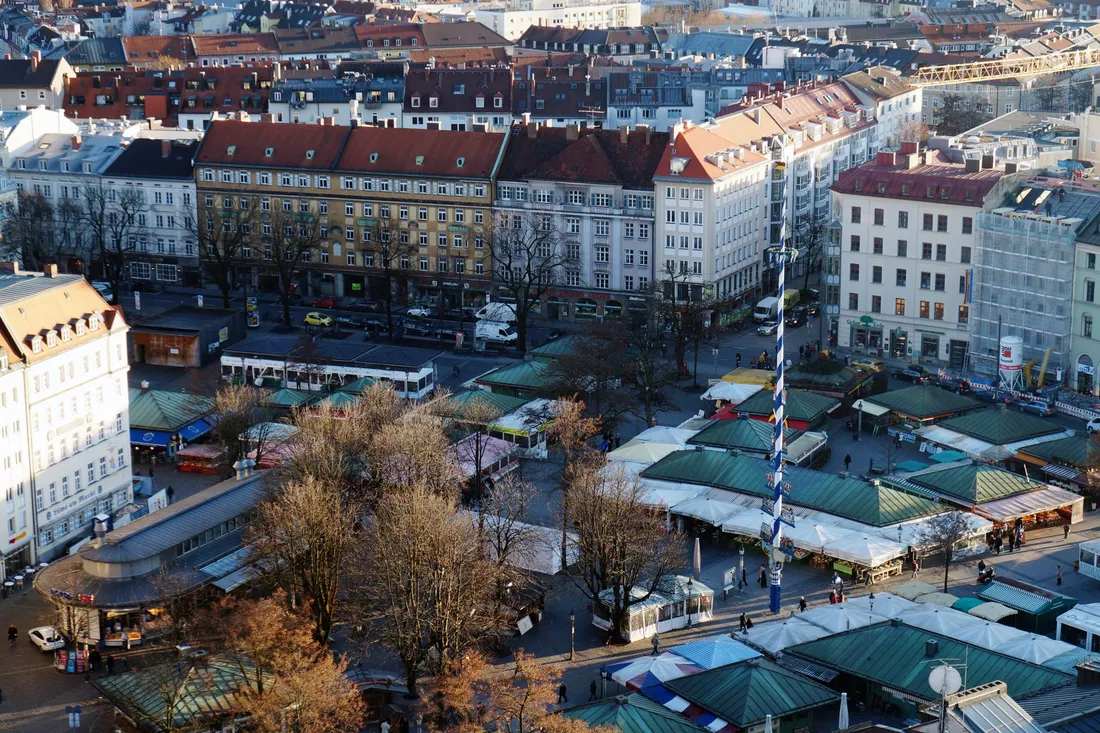 Blick von oben auf Marktstände mit grünen Dächern und einen blau-weißen Maibaum