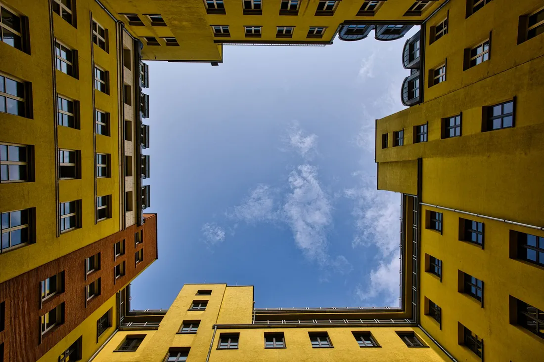 Blick aus einem gelb verputzten Innenhof senkrecht nach oben in den Himmel